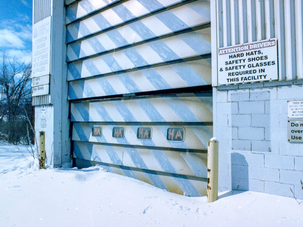 colour outdoor photo of a disused industrial size door. Snow covers the ground outside.