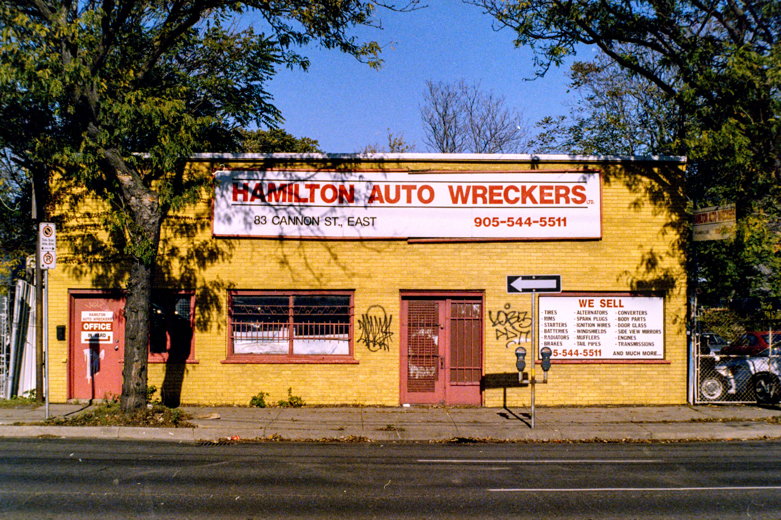 colour photo of a single storey brick building painted bright yellow. Prominent sign reads "Hamilton Auto Wreckers"