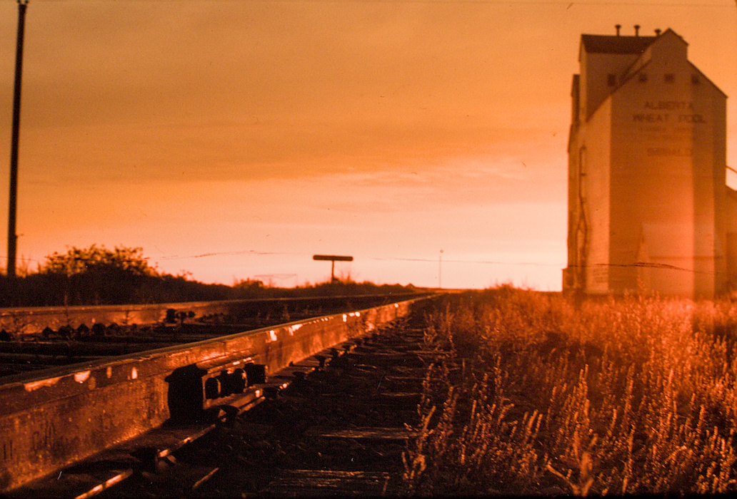 colour photo of train tracks in reddish light with grain elevator in background