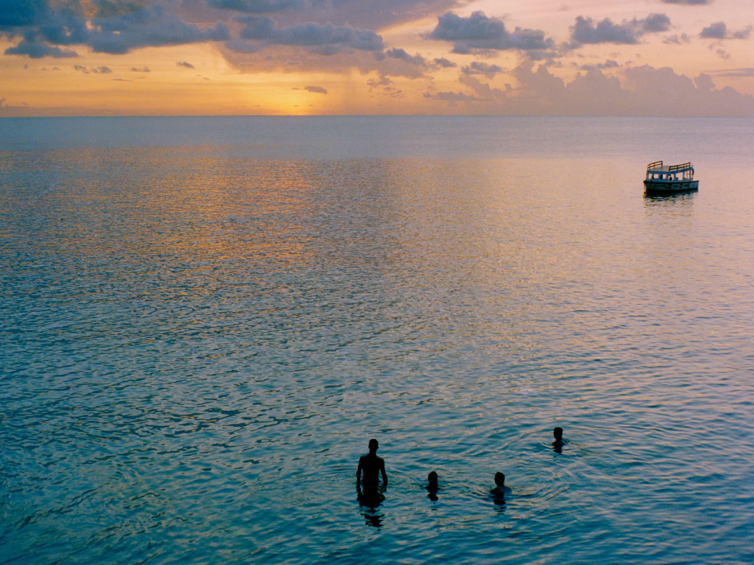 colour photo of the sunset over a calm ocean with bathers in the foreground