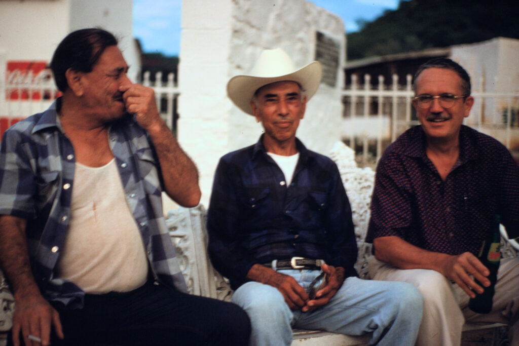 colour photo of three men sitting outdoors and smiling in conversation