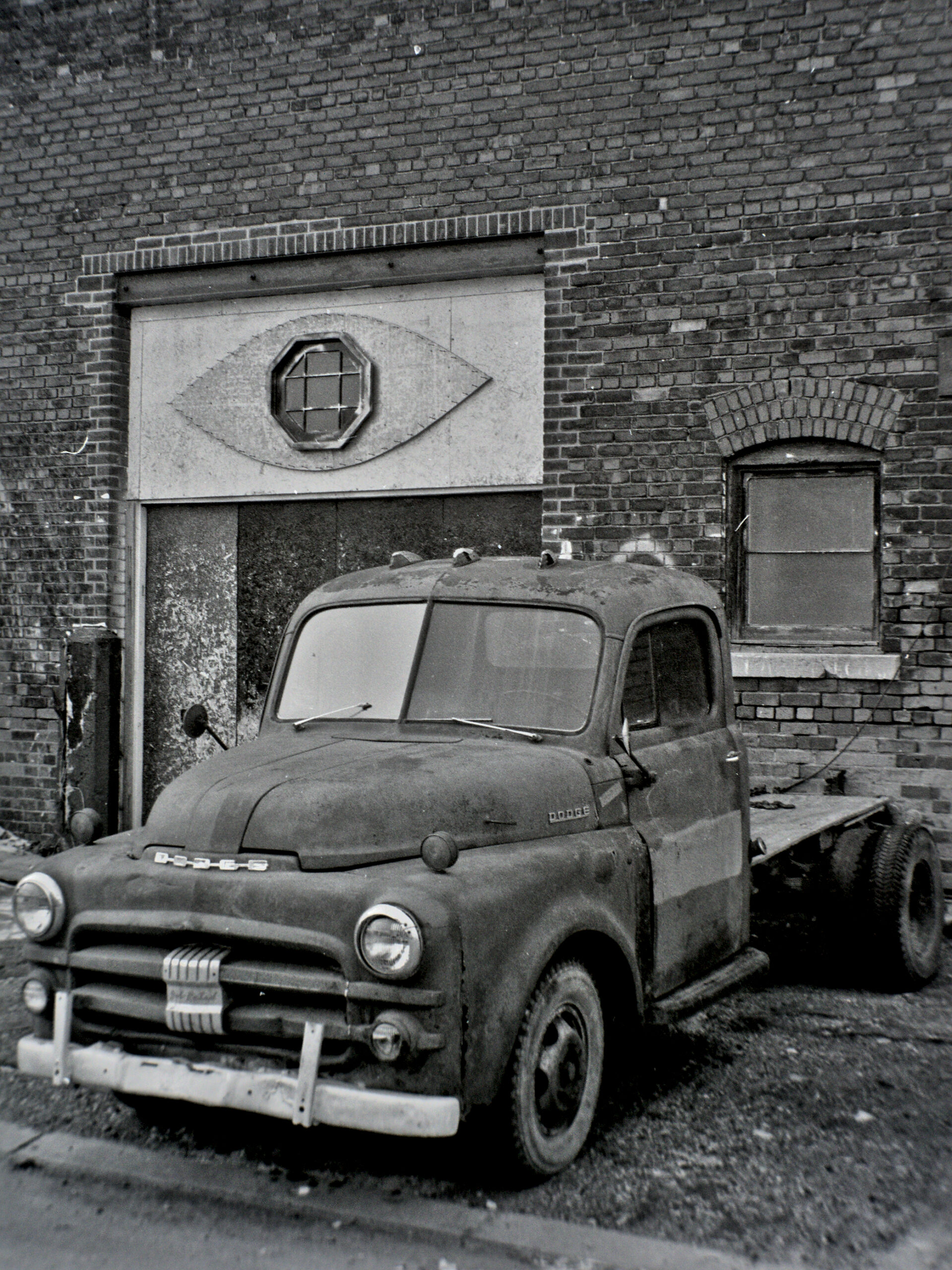 black and white photo of classic pickup truck parked in front of a brick wall