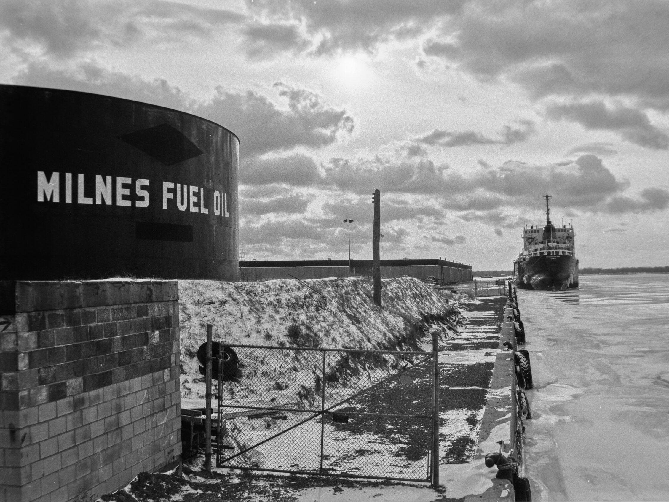 black and white photo of a large storage tank next to ship channel