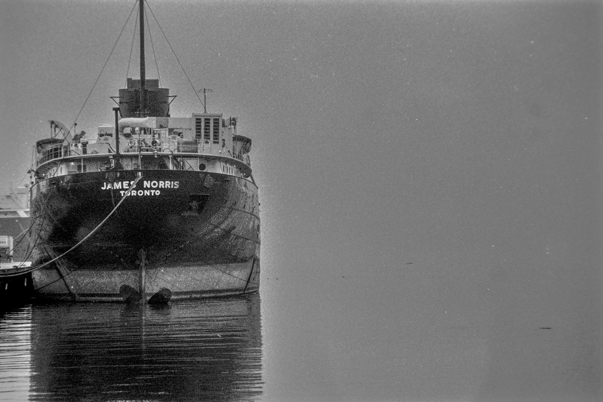 black and white photo of a cargo ship moored in thick fog. Ship name on stern "James Norris, Toronto".