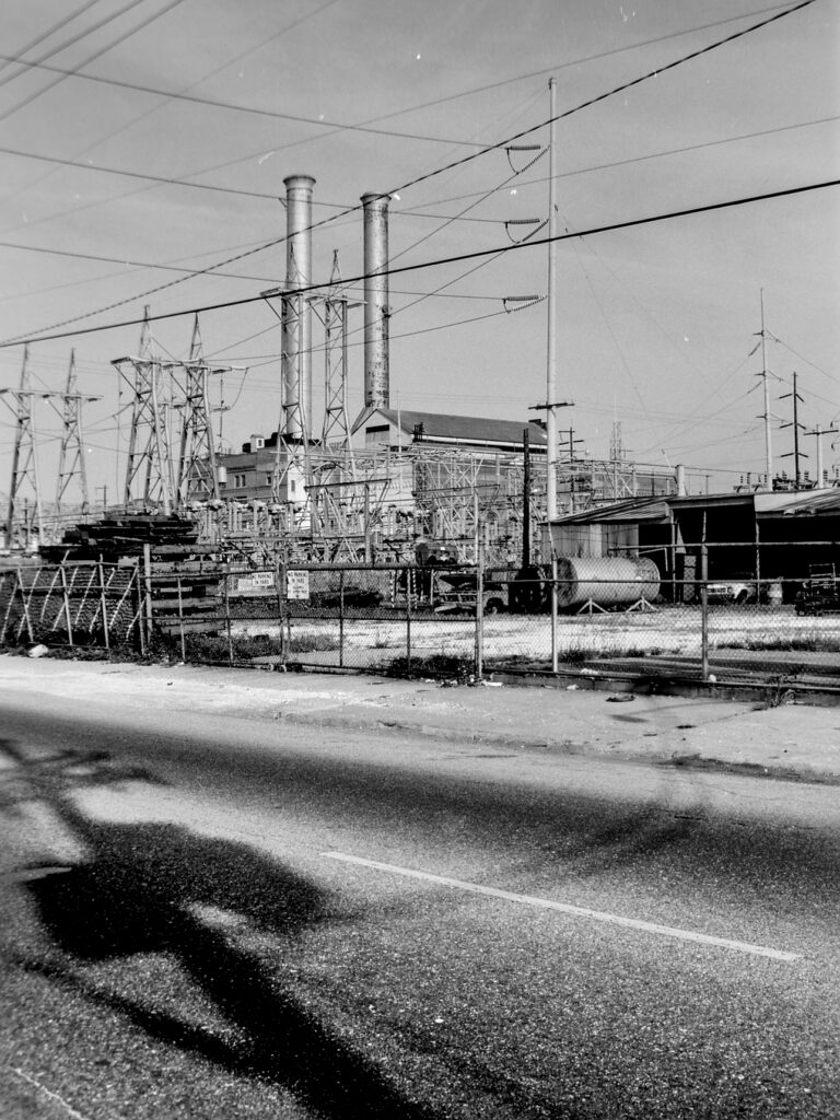 black and white photo of power tranmission lines with smokestacks in background