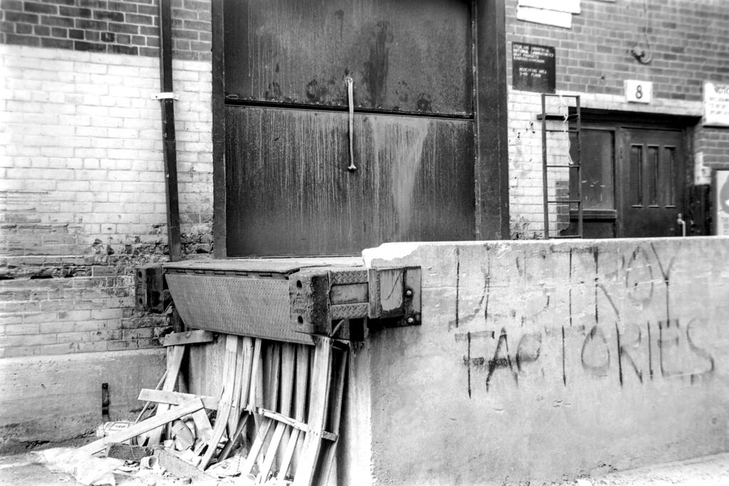 black and white photo of loading dock. graffiti on wall reads "destroy factories"