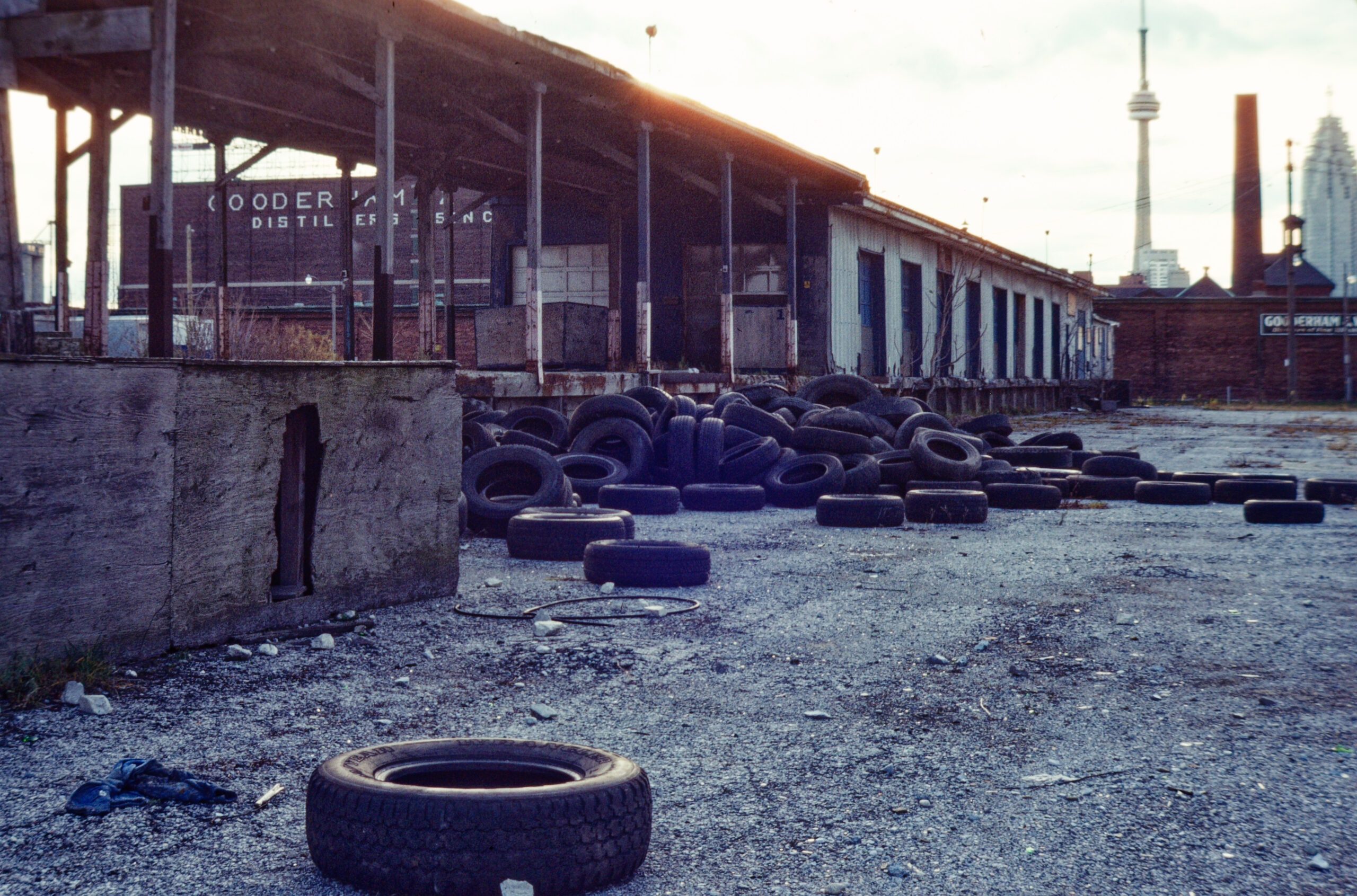 colour photo of tires piled next to abandoned loading dock with CN tower in background